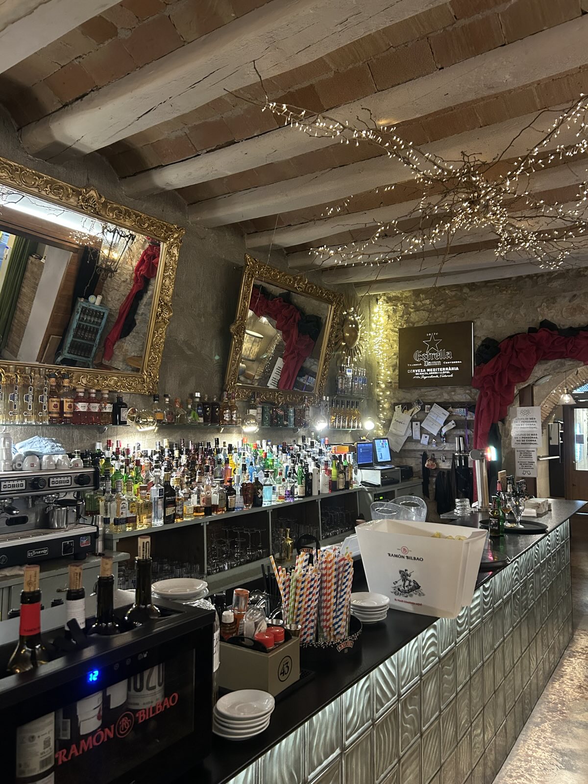 La barra: botellas, espejos dorados y vigas de madera con lucecitas