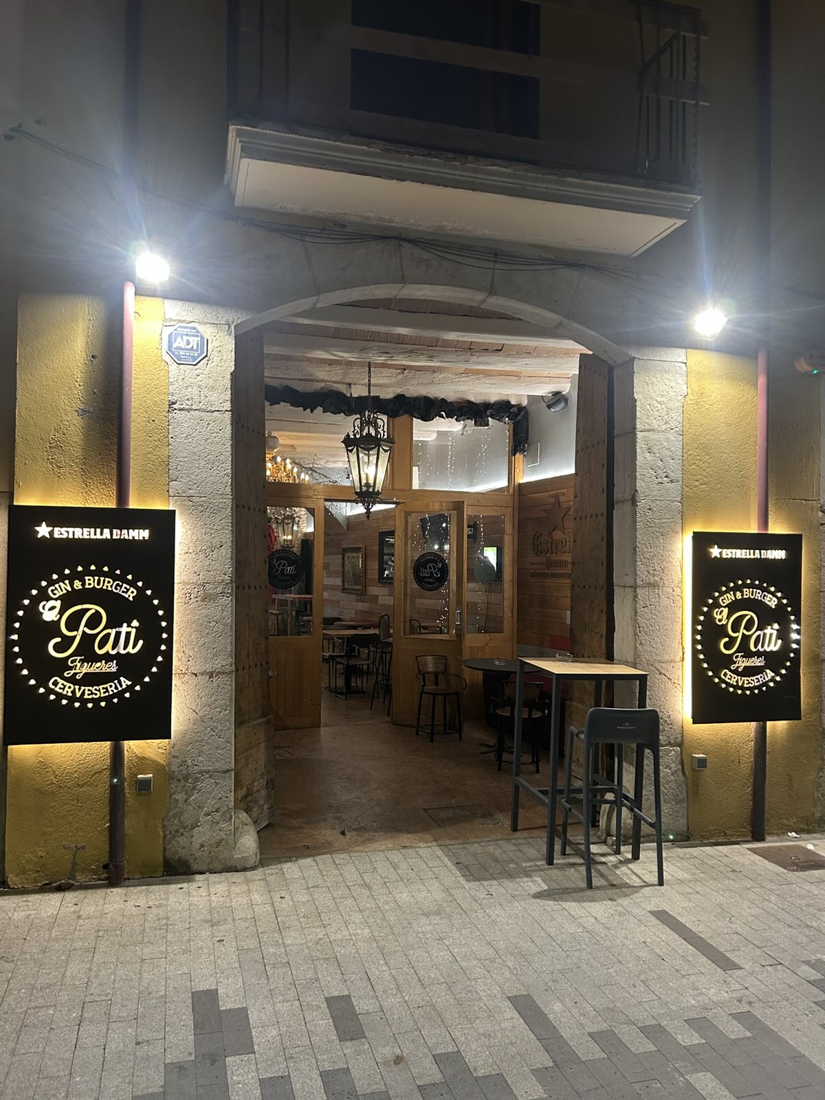 La entrada de El Pati de noche: arco de piedra y los dos rótulos iluminados