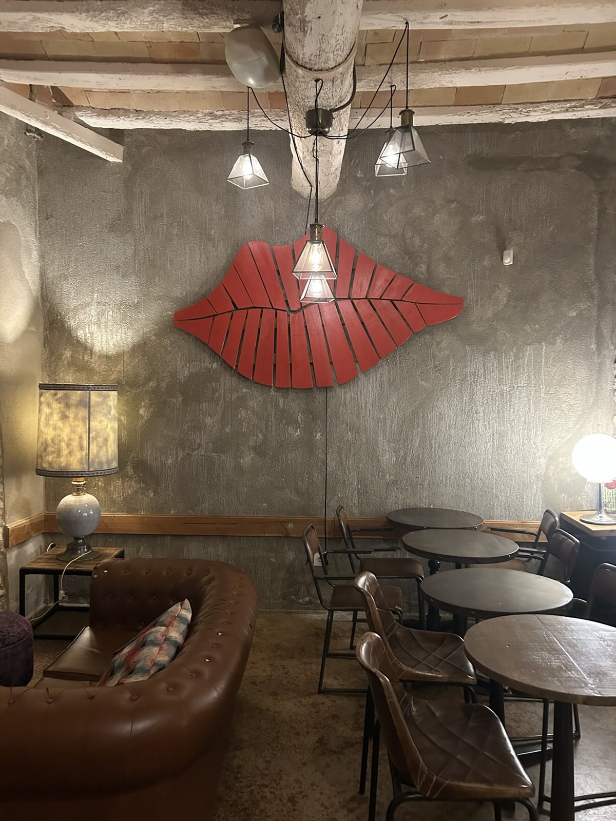 Rincón con sofá chester, mesas redondas y unos grandes labios rojos de madera en la pared