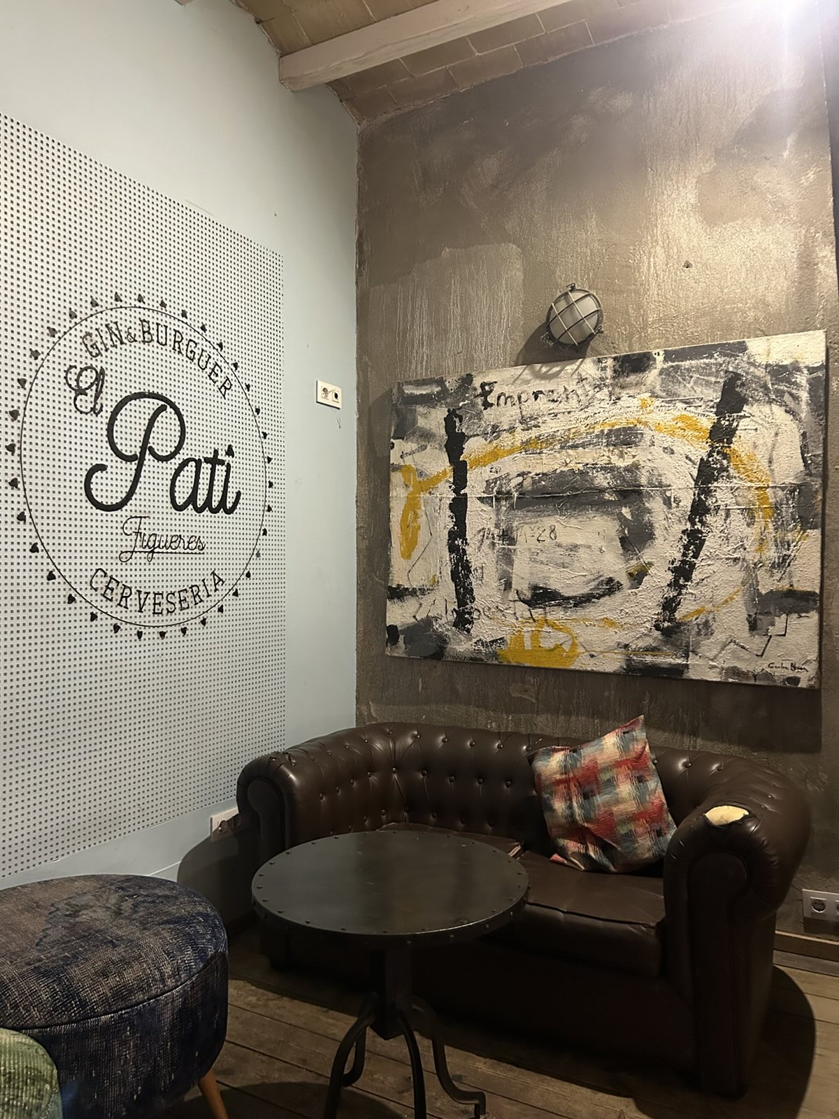 Sofá chester bajo un cuadro abstracto, junto al logotipo de El Pati pintado en la pared